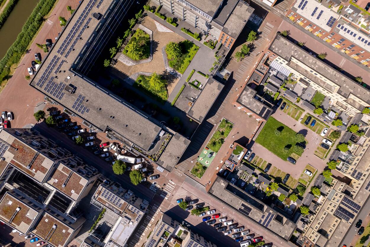 Luchtfoto van een wijk met gebouwen naast een kanaal. De foto is recht van boven genomen en toont diverse gebouwen met daartussen geparkeerde auto's, gras, bomen en in het midden een klein speeltuintje. In de linkerbovenhoek op de foto is een stukje van een kanaal te zien.